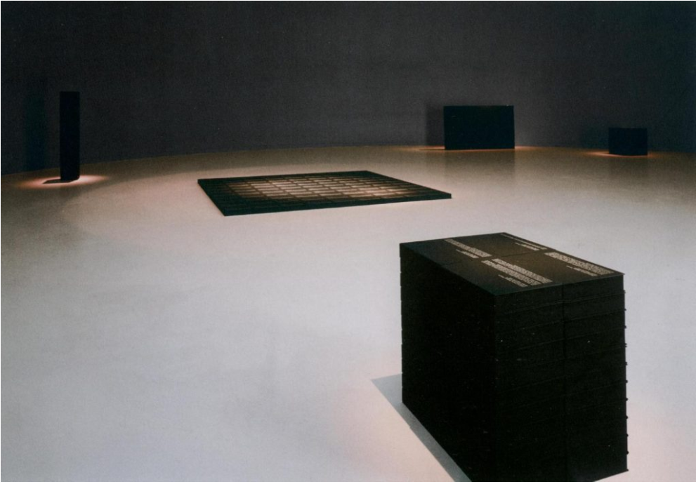 Salle d'un musée. Cube noir avec des inscriptions blanches et une grille en arrière-plan.