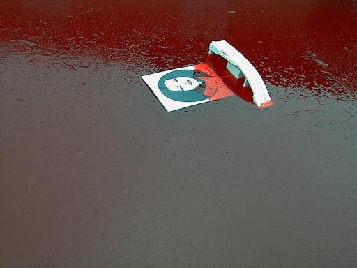 Petite photographie d'une femme tombée sur un sol qui semble humide et rougi