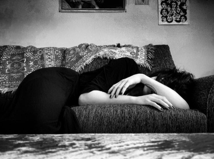 Une personne vêtue de noir étendue sur un sofa, la tête cachée par son bras.