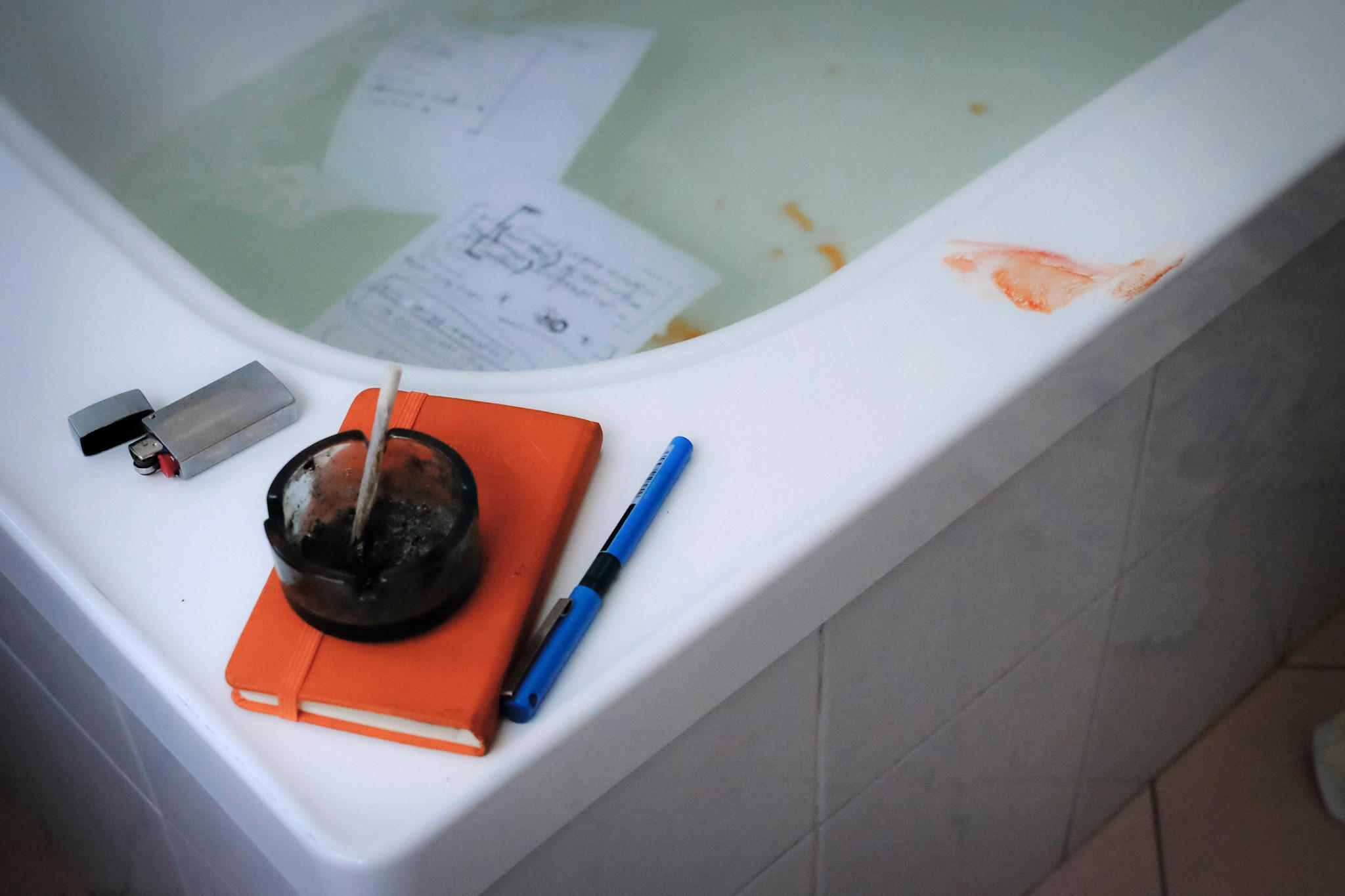 Cendrier au bord d'un bain. Des pages dans l'eau, du sang sur le rebord.